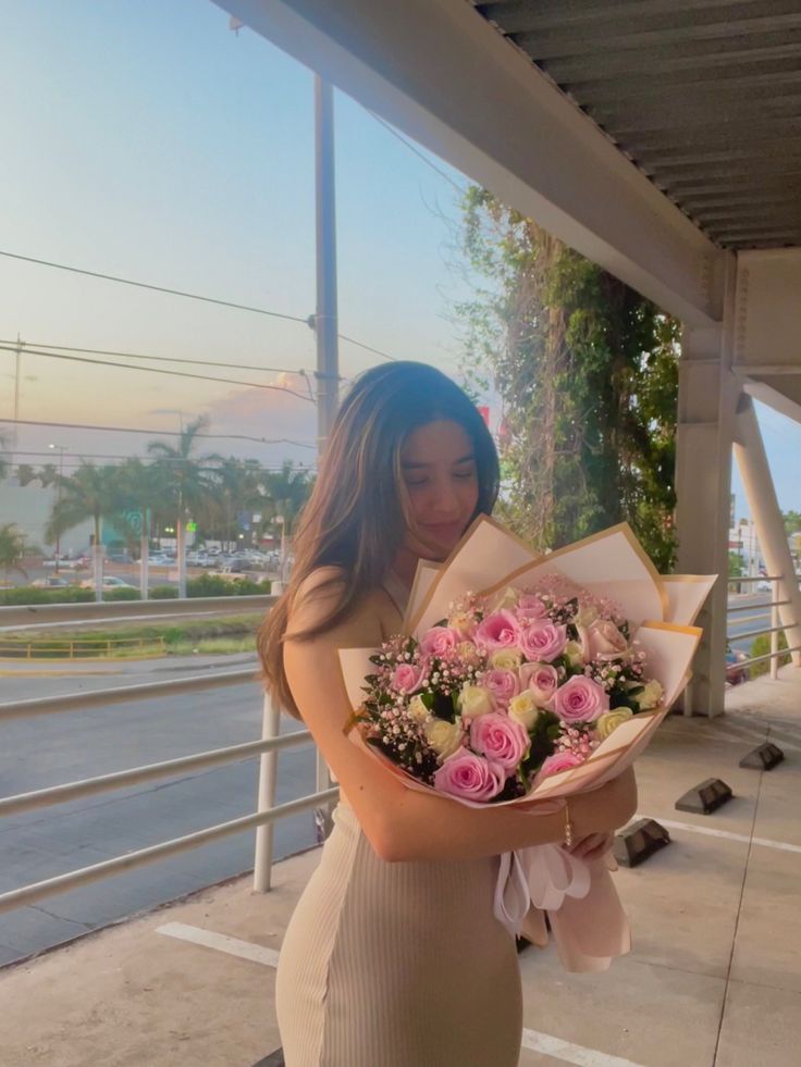 a woman holding a bouquet of pink and white flowers on the side of a road