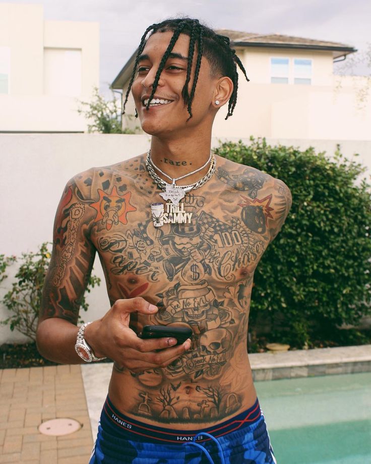 a man with tattoos on his chest holding a cell phone in front of a pool