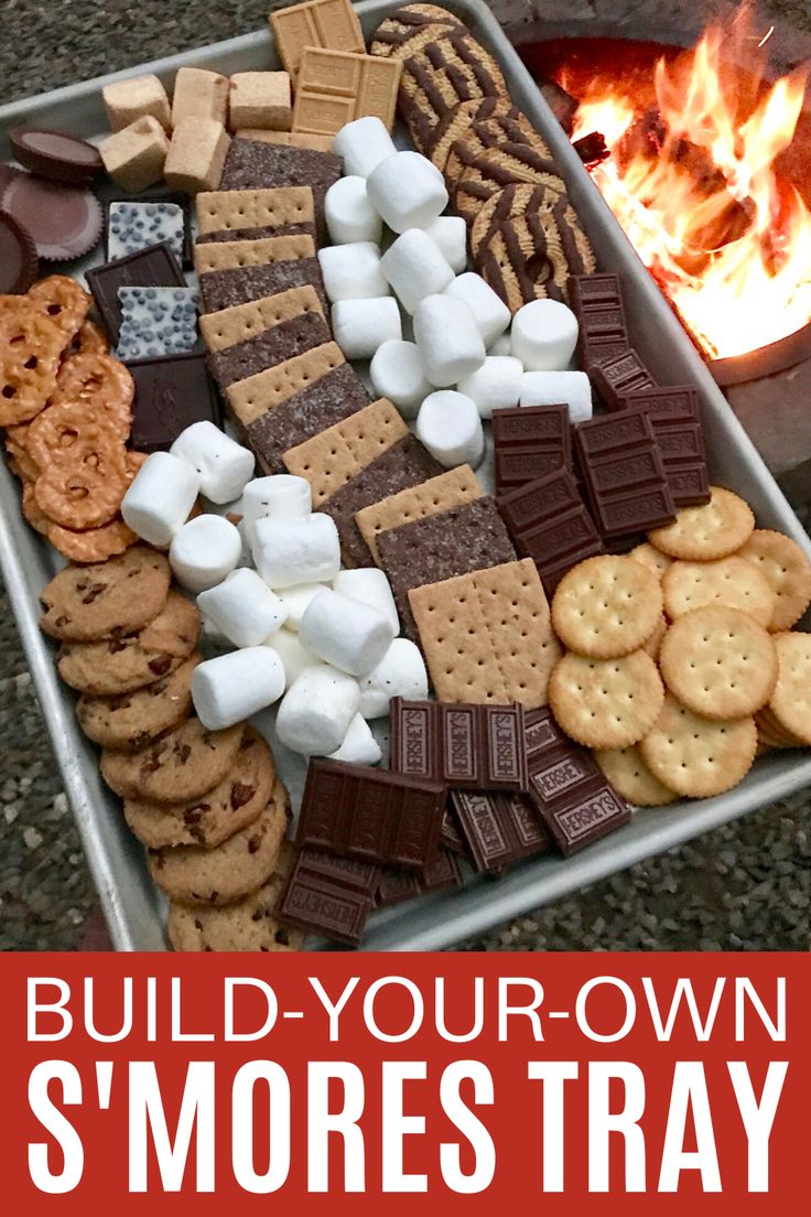 a metal tray filled with marshmallows and crackers next to a fire