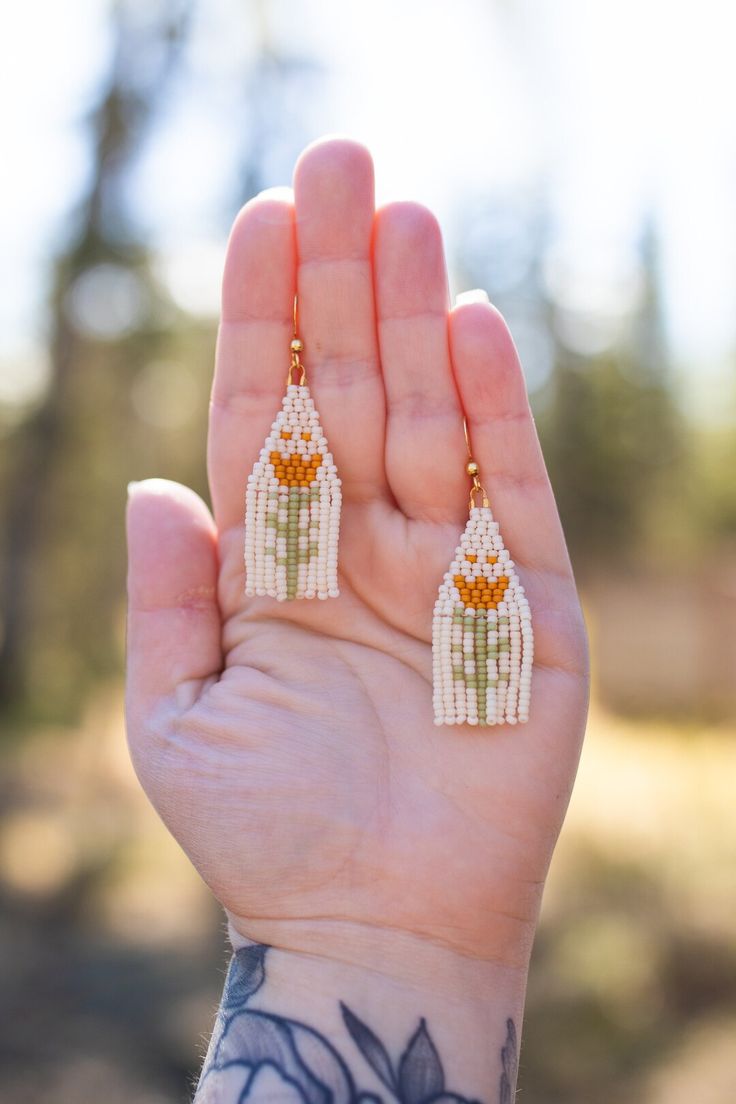 a person with tattoos holding their hand up to the camera while wearing small white and orange beaded earrings