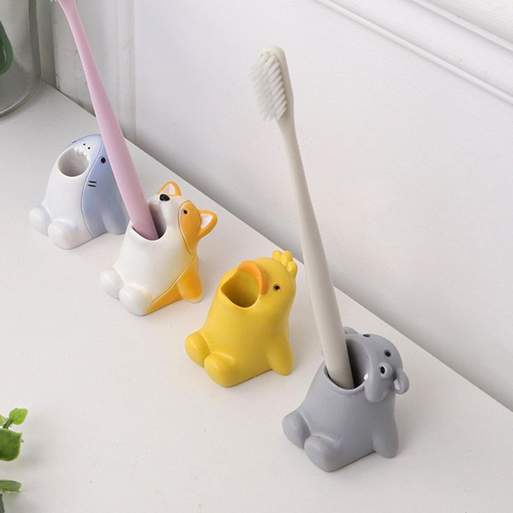 three toothbrush holders in the shape of elephants and giraffes on a counter