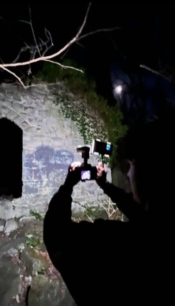 a man taking a photo with his cell phone in the dark by a stone wall