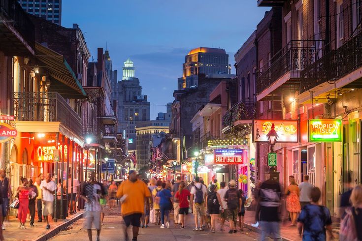 people are walking down the street in an old city at night with tall buildings on either side