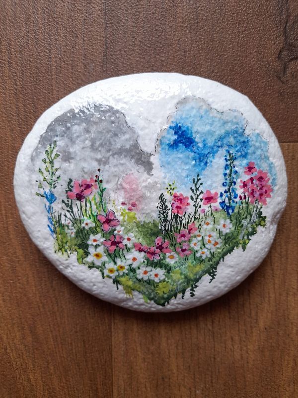 a painted rock with flowers and clouds on it