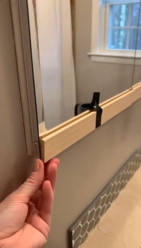 a hand is holding the edge of a mirror in front of a window with a black handle