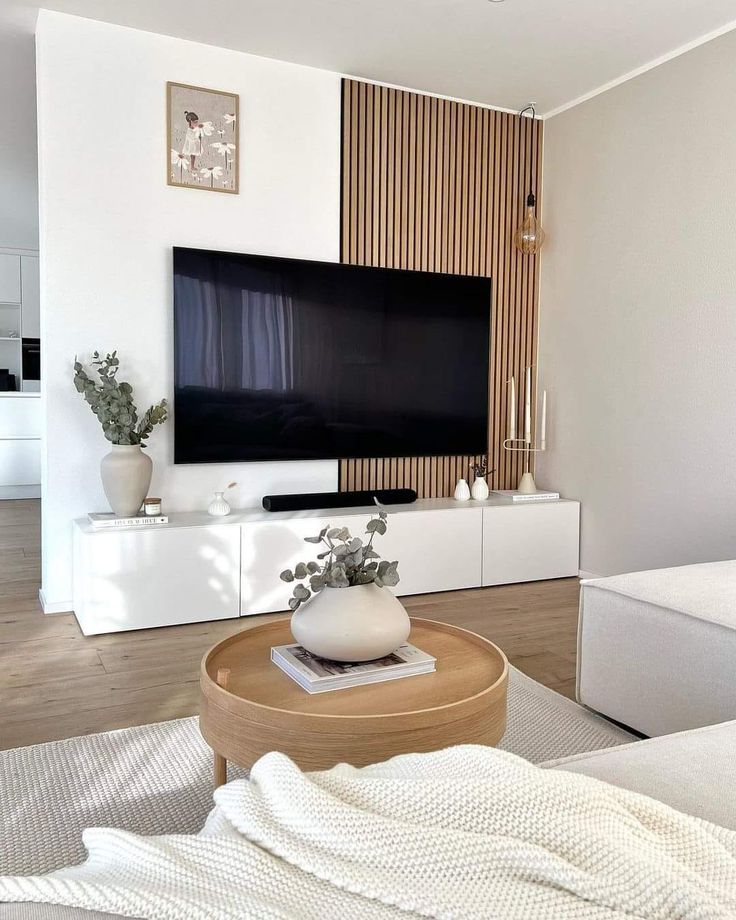 a living room with a large flat screen tv on the wall and white furniture in front of it