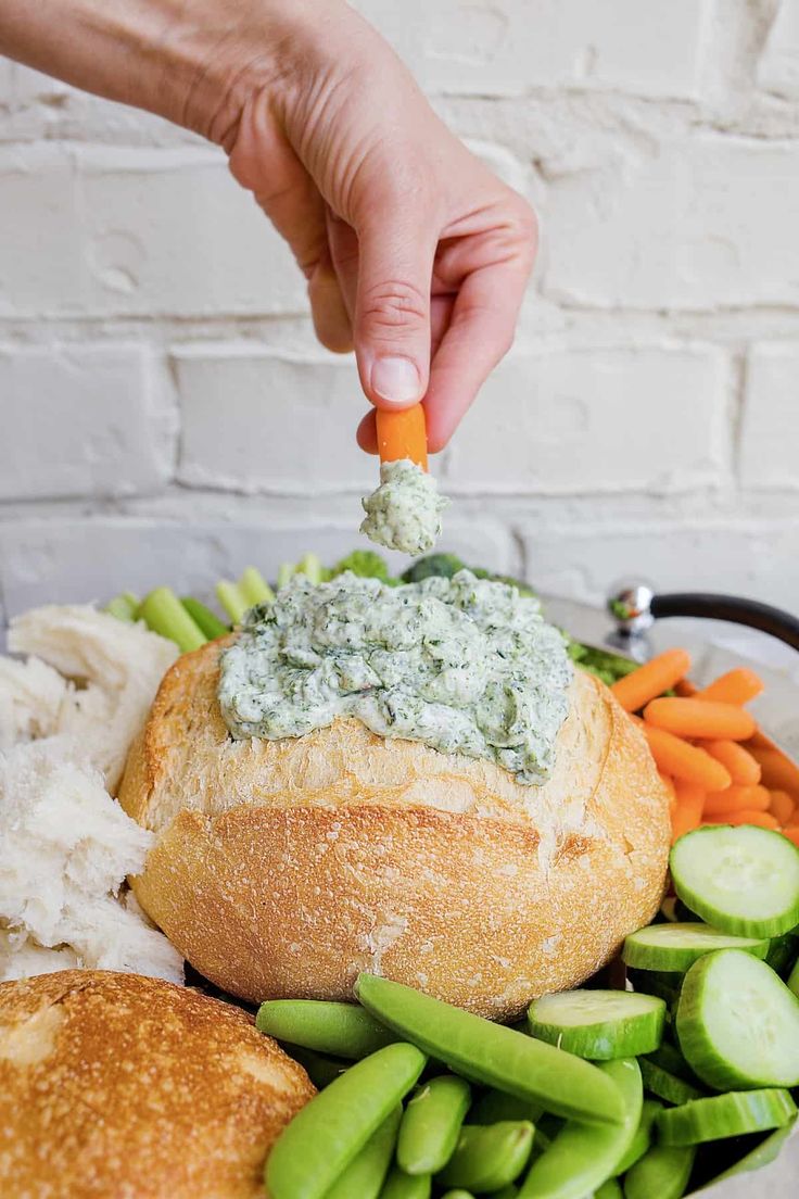 a person dipping dip into a bread bowl filled with vegetables