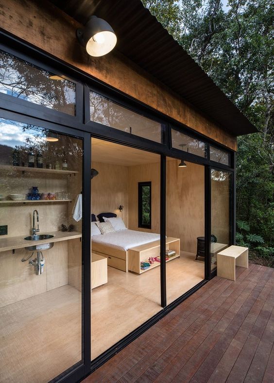 a bedroom with glass walls and wood flooring on the outside wall, overlooking a wooded area