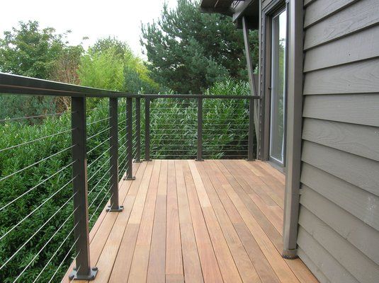 a wooden deck with metal railings and trees in the background