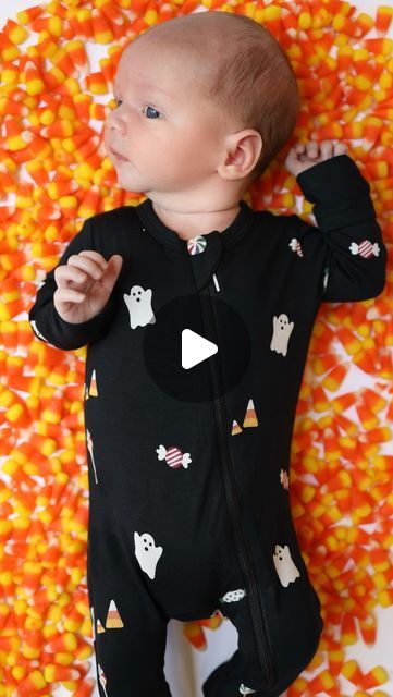 a baby laying on top of candy corn wearing a black onesie with ghost and pumpkins all over it