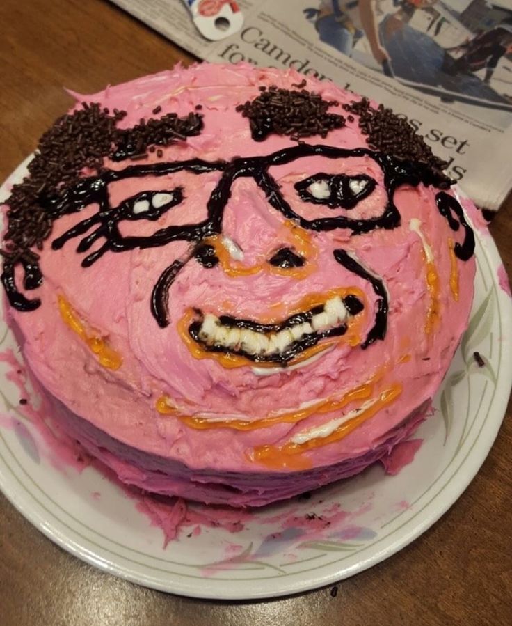 there is a pink cake with black icing on it and a face drawn on the top