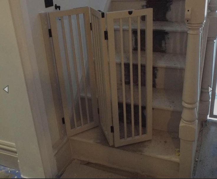 a baby gate sitting in the corner of a room next to a stair case and window