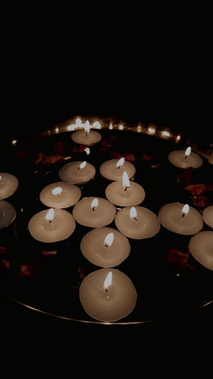 many lit candles in a metal pan on a black surface with one candle turned upside down