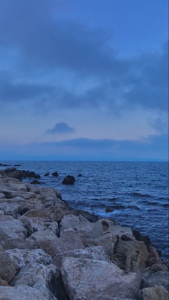 a person standing on rocks near the ocean with an umbrella in their hand and looking out at the water