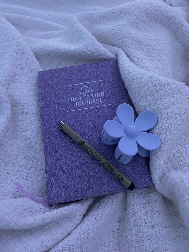 a purple book with a flower on it next to a pen and eraser laying on a bed