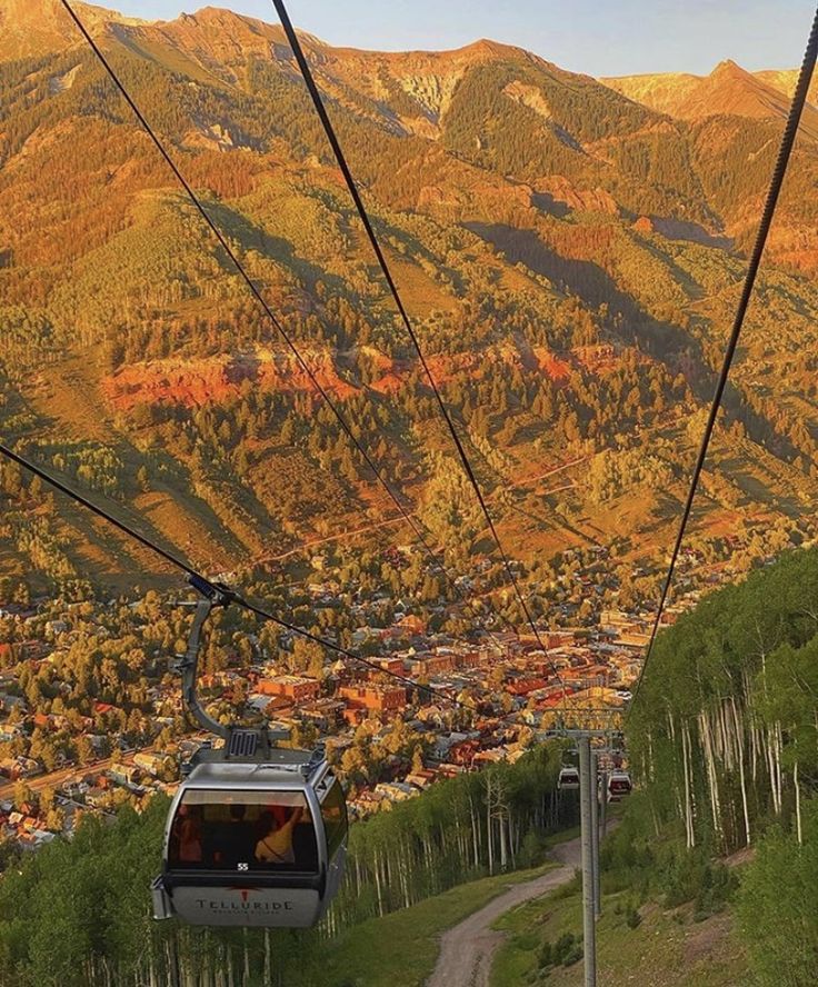 a ski lift going up the side of a mountain with trees and houses on it