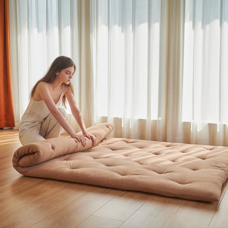 a woman sitting on top of a mattress in the middle of a room with curtains