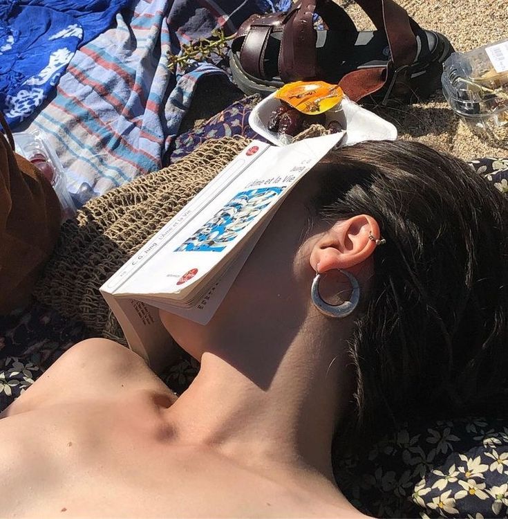 a woman laying on top of a beach next to a bag