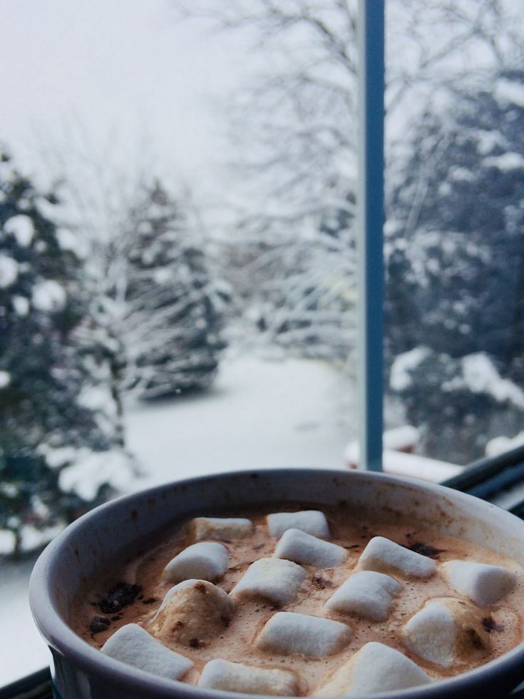 a cup of hot chocolate with marshmallows in it sitting on a window sill