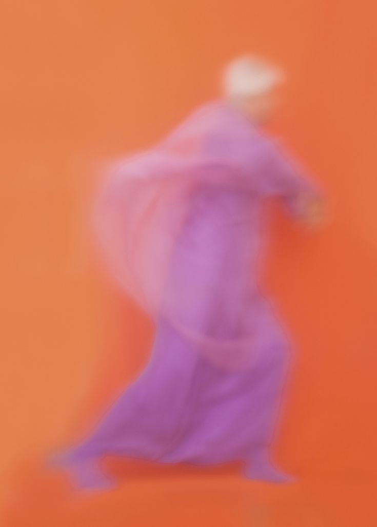 a blurry image of a woman in a long purple dress dancing on an orange background