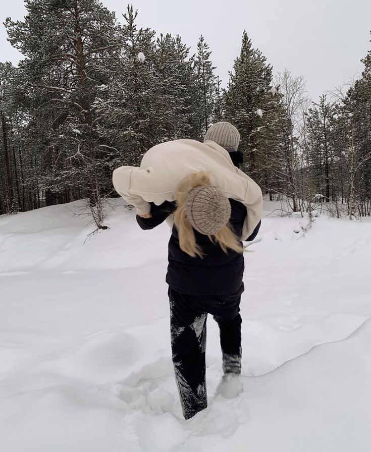 a person walking in the snow carrying a teddy bear on their back and wearing a hat