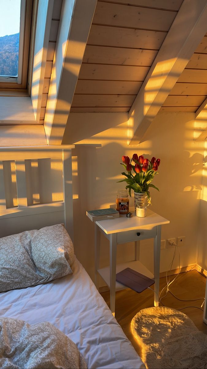 a small white bed sitting under a window next to a table with flowers on it