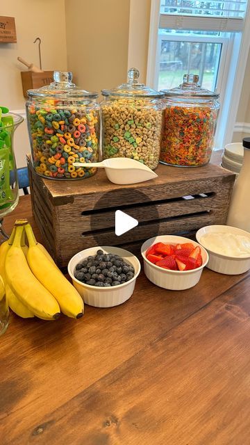 a wooden table topped with bowls filled with fruit and cereal next to jars full of candy