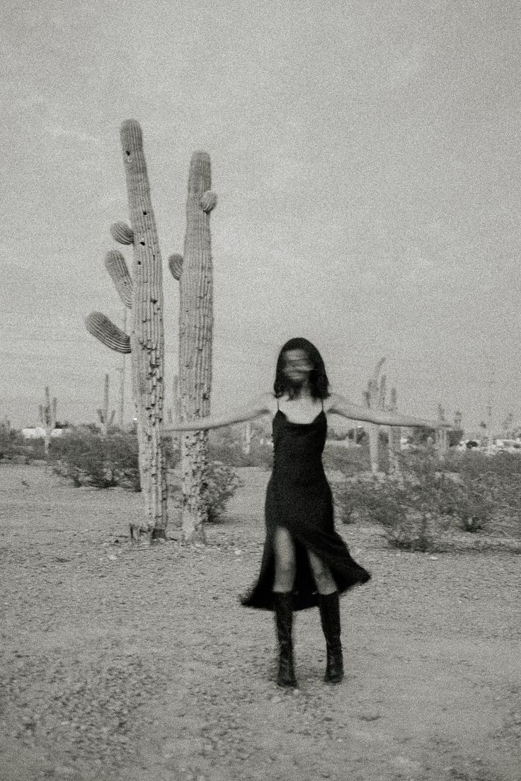 a woman standing in front of a tall cactus with her arms outstretched and legs crossed