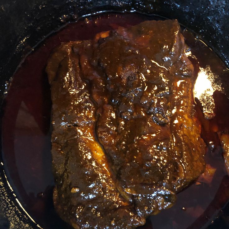 a piece of meat covered in gravy sitting on top of a pan filled with sauce