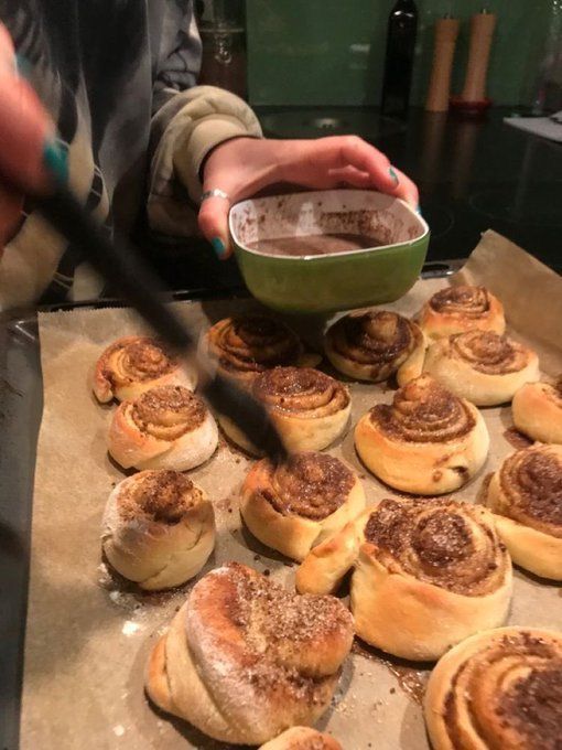 some cinnamon rolls are sitting on a baking sheet and someone is holding a bowl with something in it