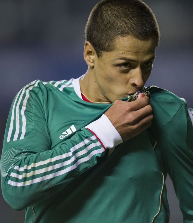 a man in green jersey eating something with his hand on his mouth and looking at the camera