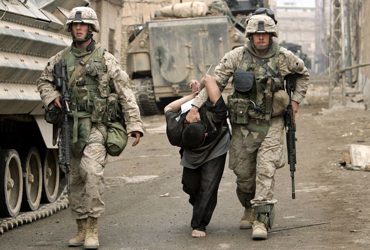 two soldiers walking down the street with an injured man on his back and another soldier carrying him