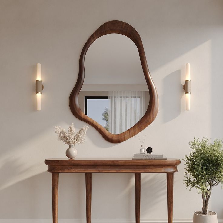 a mirror on the wall above a wooden table with vase and potted plant next to it