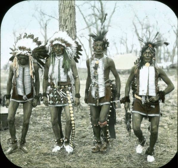 three native american men standing next to each other in front of a tree and grass field