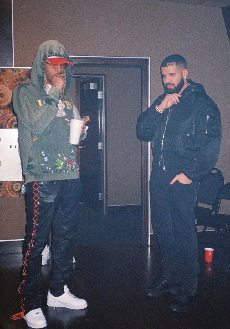 two men standing next to each other in front of a door and one holding a cup