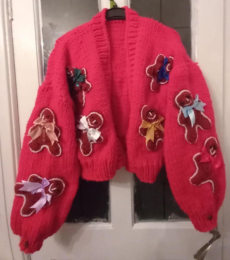 a pink sweater with bows and sequins hanging on a door