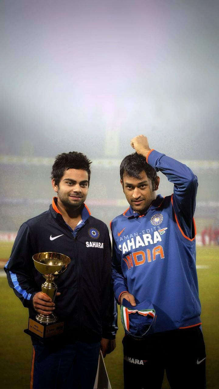 two men standing next to each other on a field with a trophy in their hands