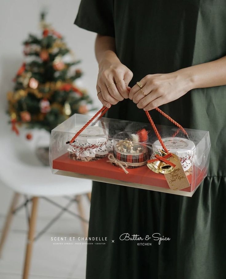 a woman is holding a red box with christmas decorations on it and tied in twine