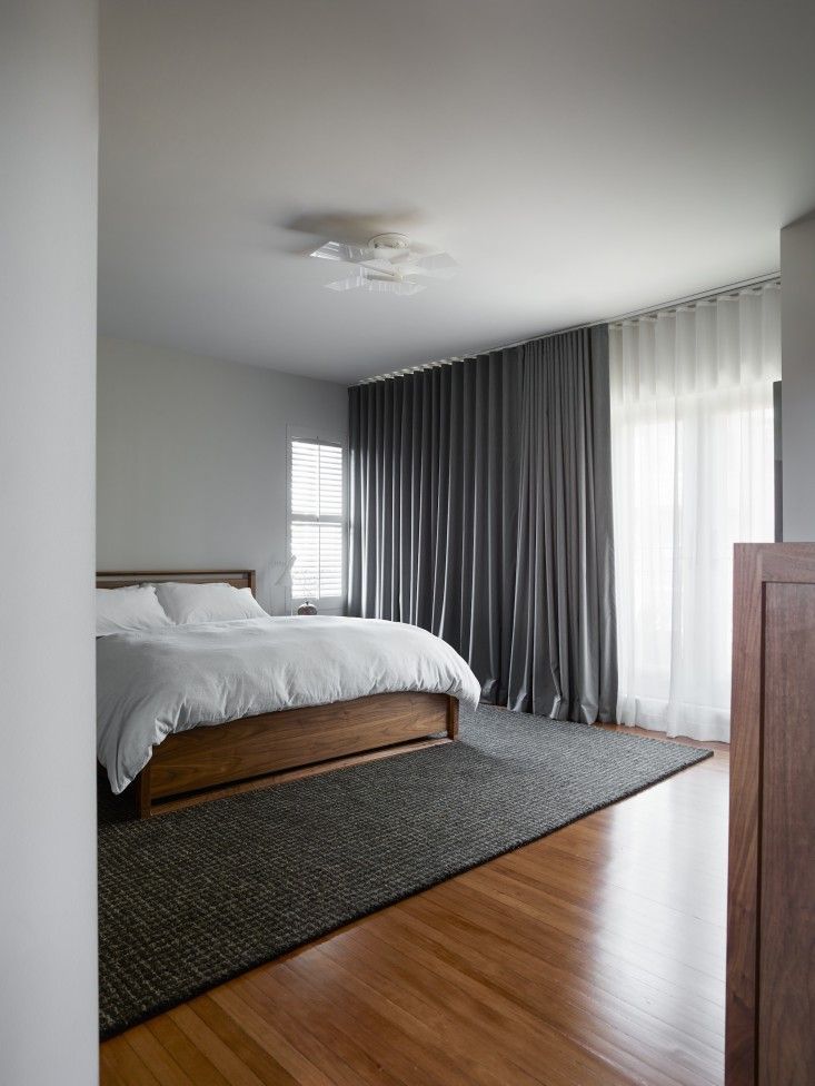 a bedroom with hardwood floors and white bed in the middle, along with curtains on the windows