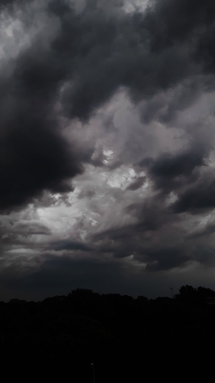 the sky is filled with dark clouds and some trees