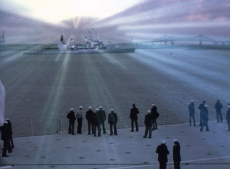 a group of people standing in front of a large ship on the water with beams of light coming from it