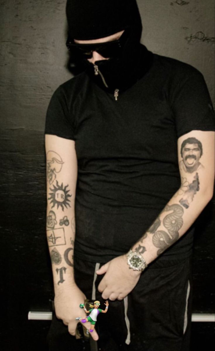 a man with tattoos on his arm and face holding an object in one hand while wearing a black hoodie