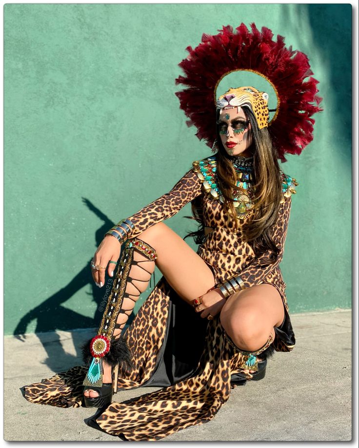 a woman in a leopard print dress and headdress sitting on the ground with her legs crossed