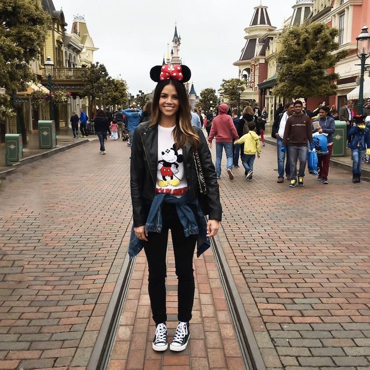 a woman standing on a brick walkway in front of buildings wearing minnie mouse ears and a t - shirt