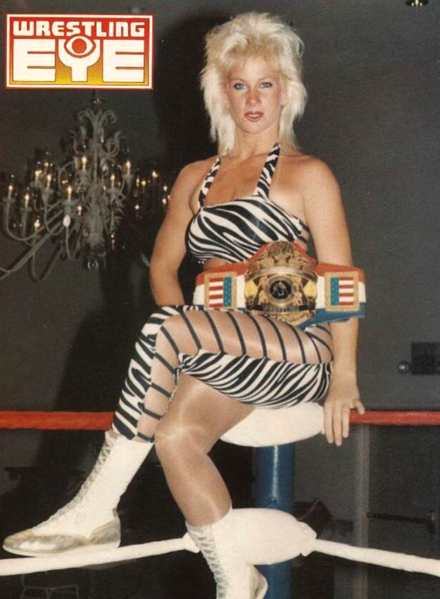 a woman sitting on top of a pole in a wrestling ring holding a wrestler's belt