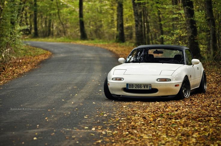 a white sports car parked on the side of a road in front of some trees