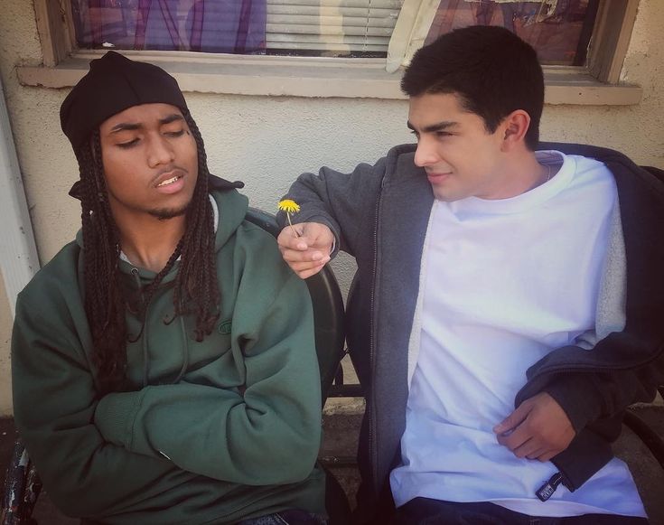 two young men sitting on a bench and one is holding a flower in his hand