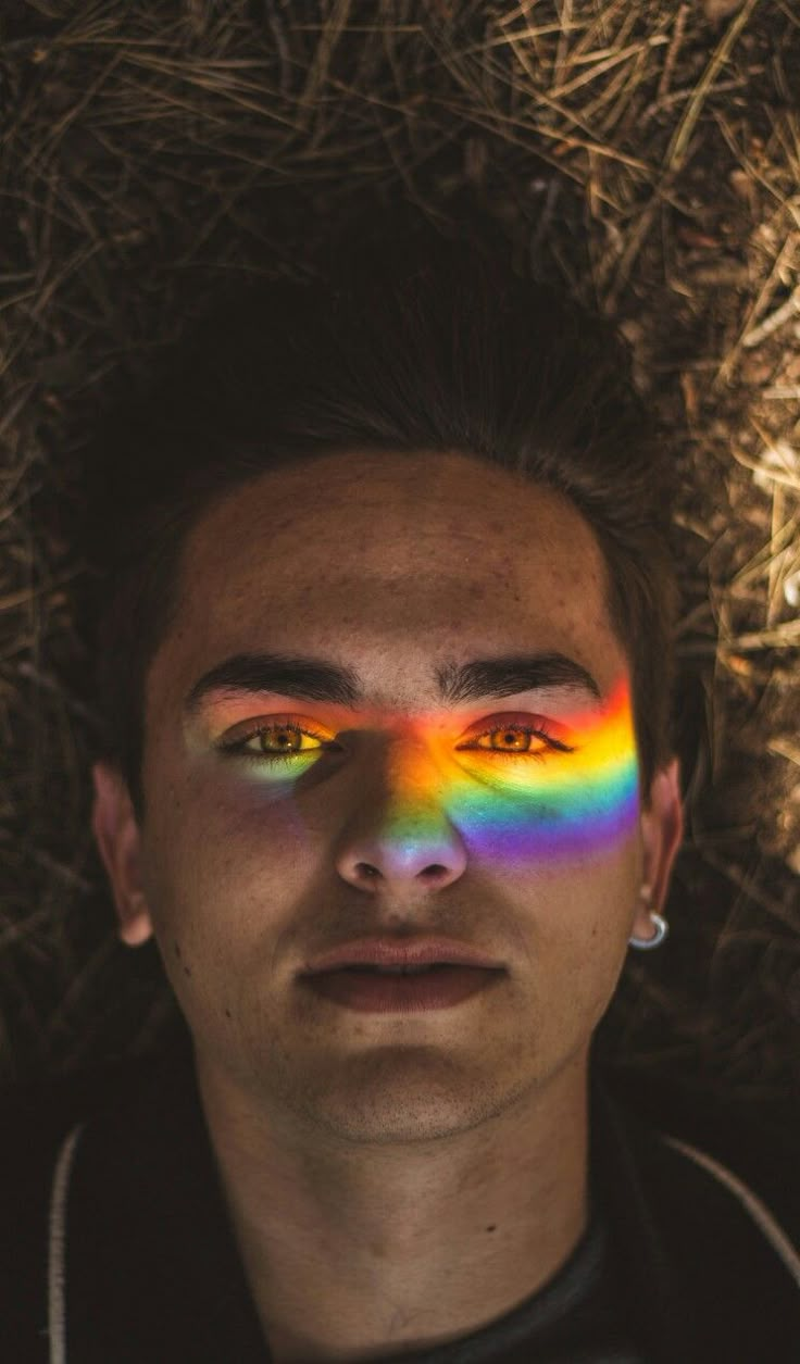 a man with rainbow painted on his face laying in the hay looking at the camera