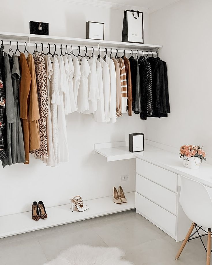 an organized closet with clothes and shoes hanging on the wall, next to a white desk