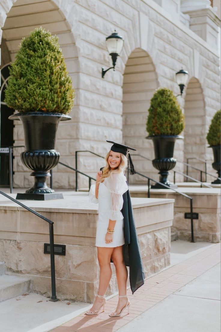 a woman wearing a graduation cap and gown standing in front of a building with her hand on her hip